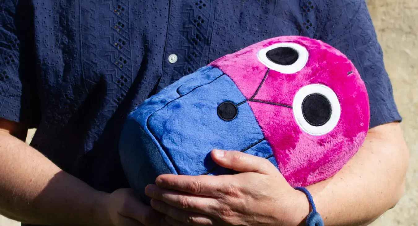 Mann hält ein grosses iosys-Plüschmaskottchen in Pink und Blau im Arm