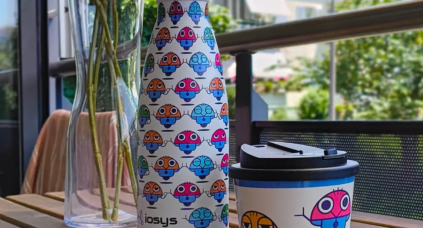iosys Trinkflasche mit Maskottchen-Rundumdruck und Kaffeebecher to go auf Balkontisch